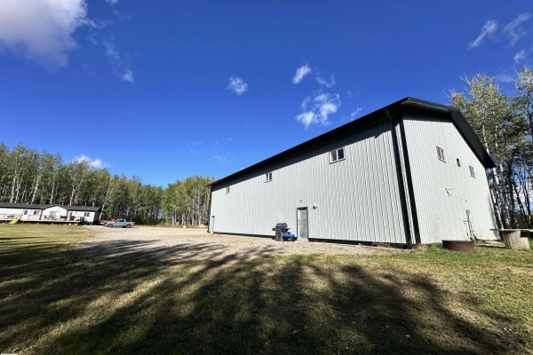 View of the long side of a large, light grey steel building with multiple windows, grass in foreground. - 7323 Twp Road 512, Rural Parkland County
