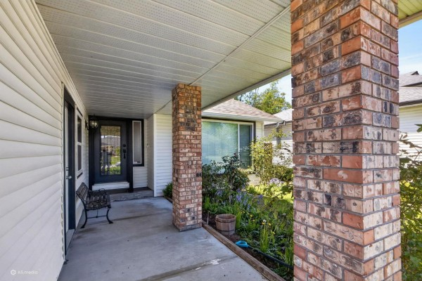 Covered front porch with white siding, brick support columns, and a dark front door with glass panels. - 7325 123 Street, Surrey