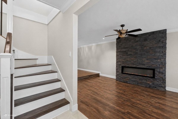 Interior view of a living room with dark wood floors, a raised platform, and a modern fireplace with stone surround. - 7325 123 Street, Surrey