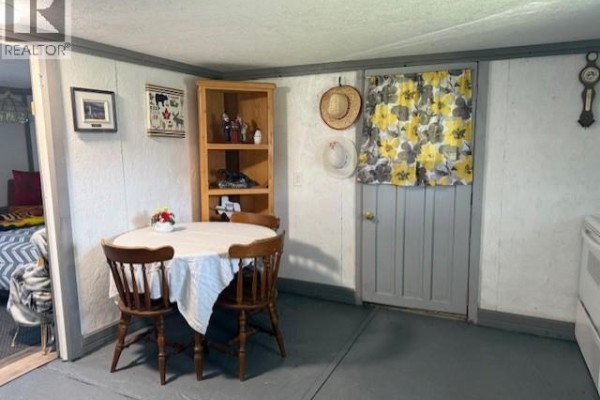 Dining area with a round table, two wooden chairs, and a door with floral curtains. - 7344 Route 117, Miramichi Bay