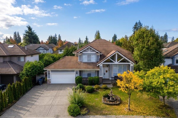 Two-story grey house with brown roof, attached garage, and landscaped front yard under a blue sky. - 7355 146a Street, Surrey