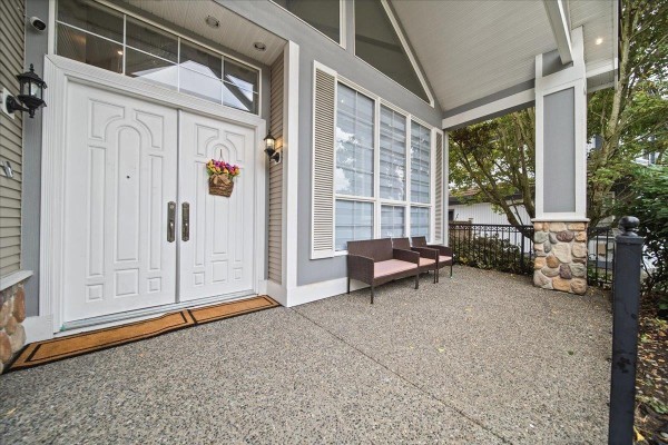 Close-up of a covered front porch with double white doors, windows, and seating. - 7355 146a Street, Surrey