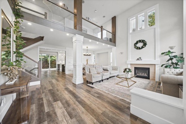 Spacious living area with vaulted ceiling, fireplace, staircase, and view of dining and kitchen areas. - 7355 146a Street, Surrey