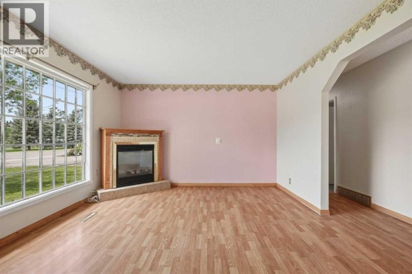 Living room featuring a fireplace with a wood mantel and a large bay window. - 736 2 Street W, Cardston