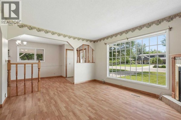 Living room with a large bay window, wood laminate flooring, and an arched doorway. - 736 2 Street W, Cardston