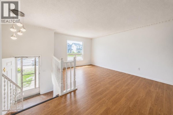 Interior view of a spacious living room with wood floors, white walls, a large window, and a view of the staircase. - 7363 59 Avenue, Red Deer
