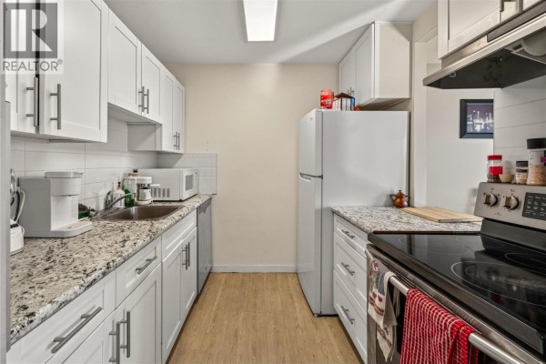 Galley kitchen with white cabinets, granite countertops, and stainless steel appliances. - 737 Leon Avenue Unit# 1007, Kelowna