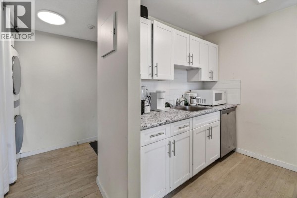 Compact kitchen with white cabinets and light wood-look flooring, next to laundry area. - 737 Leon Avenue Unit# 1007, Kelowna