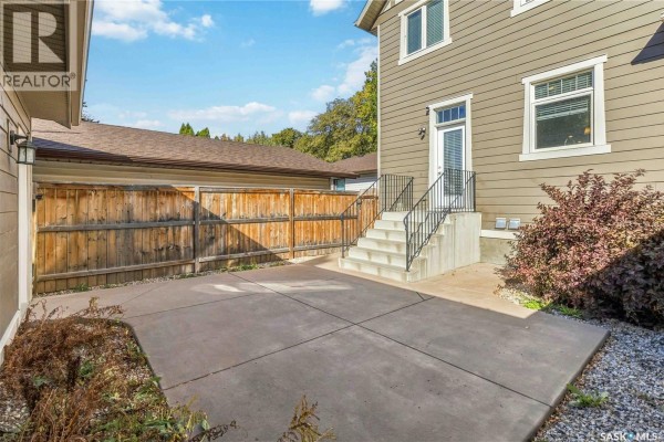Concrete backyard patio with a wooden fence and exterior stairs leading to a back door. - 738 4th E, Saskatoon