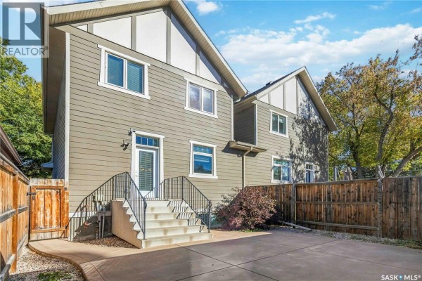 Rear view of a two-story house with beige siding, windows, and a concrete patio. - 738 4th E, Saskatoon