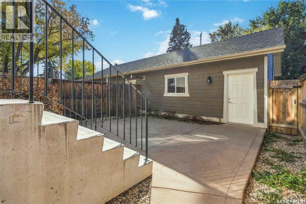 Concrete steps with a metal railing leading to a side door of a house with a fenced yard. - 738 4th E, Saskatoon