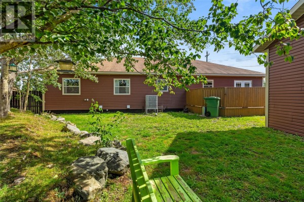 Backyard view of the red house with a green bench, lawn, and wooden fence. - 738-742 Ville Marie Drive, Marystown