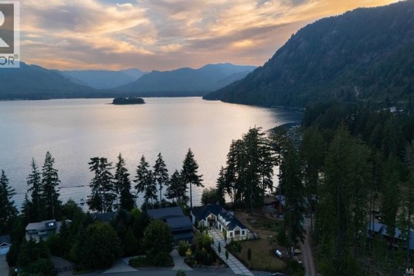Aerial view of a modern white house with a dark roof on a wooded lakefront property. - 7380 Lakefront Dr, Lake Cowichan