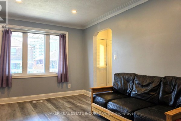 Living room with grey walls, hardwood floors, and a black leather sofa facing a large window. - 739 Vaughan Road, Toronto