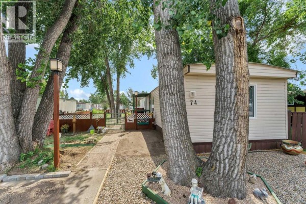 Side entrance of a mobile home with a pathway, fence, and decorative garden elements. - 74, 4000 13 Avenue Se, Medicine Hat