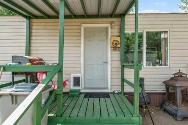 Close-up of a green wooden porch on a mobile home with a white door and windows. - 74, 4000 13 Avenue Se, Medicine Hat