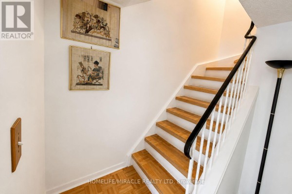 Staircase with natural wood treads, white risers, black handrail, and framed artwork on the wall. - 74 - 2651 Aquitaine Avenue, Mississauga
