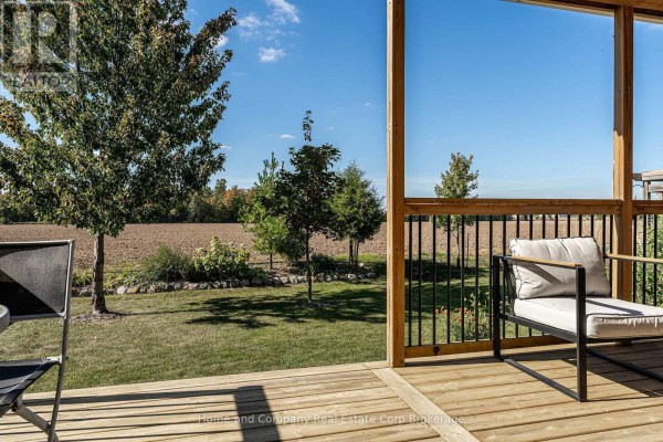 Wooden deck overlooking a grassy backyard with scattered trees and agricultural fields under a blue sky. - 74 Ahrens Drive, Stratford