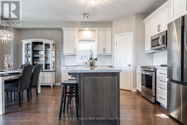 Modern kitchen with white cabinets, a large island with a dark wood base, and stainless steel appliances. - 74 Ahrens Drive, Stratford