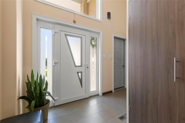 Front entrance with a white door featuring geometric glass inserts and a plant. - 74 Breezy Bend, Steinbach