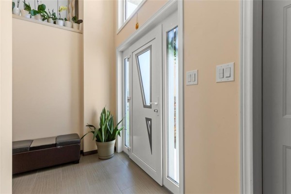 Foyer with a white door, plant, bench, and smooth beige walls. - 74 Breezy Bend, Steinbach