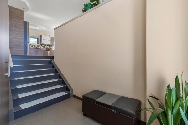 Interior view showing a staircase with dark grey steps leading up to a kitchen area. - 74 Breezy Bend, Steinbach