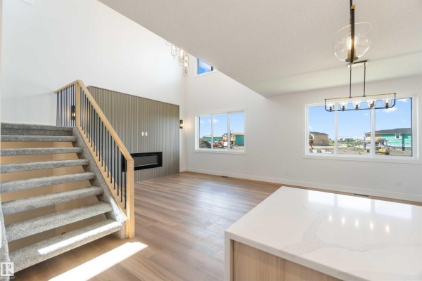 Living room with a high ceiling, gas fireplace, large windows, and light wood flooring. - 74 Eldridge Pt, St  Albert
