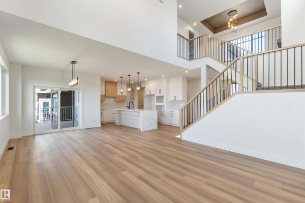 Spacious open-concept living area with a kitchen island, staircase, and sliding glass doors to a deck. - 74 Eldridge Pt, St  Albert