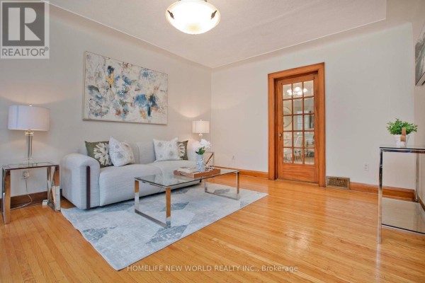 Living room with a light gray sofa, glass coffee table, and hardwood floors. - 74 Haddon Avenue N, Hamilton