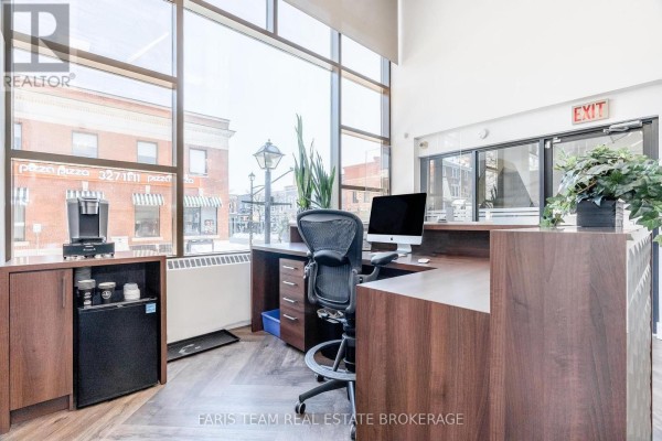 Conference room with a large wooden table, black chairs, wall art, and a sideboard against the window. - 74 Mississaga Street E, Orillia