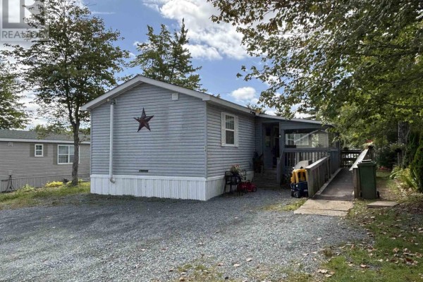 Front view of a light blue mobile home with grey siding, a ramp to the porch, and gravel driveway. - 74 Veinotte Drive, Wileville