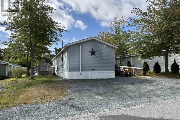Side exterior view of a light blue mobile home with grey siding and trees in the yard. - 74 Veinotte Drive, Wileville