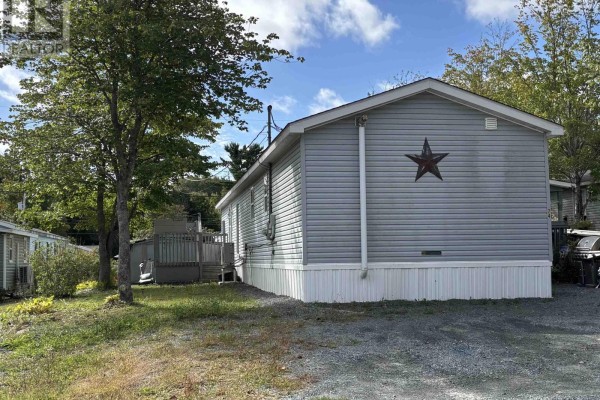 Side view of a light blue mobile home with grey siding and white trim, parked on a gravel lot. - 74 Veinotte Drive, Wileville