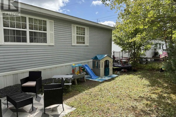 Backyard of a mobile home with outdoor seating, a child's playset, and a trampoline. - 74 Veinotte Drive, Wileville