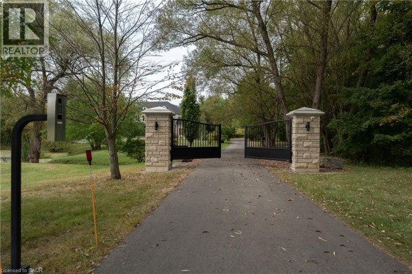 View of an open black metal gate with stone pillars and a paved driveway leading onto the property. - 740 Fiddlers Green Road, Ancaster