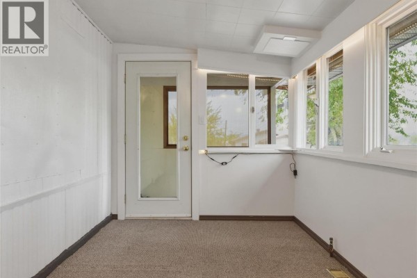 Sunroom with beige carpet, white paneled walls, and a glass door. Windows offer a green outdoor view. - 7400 Pleasant Valley Road Unit# 34, Vernon