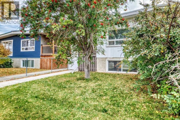 Front view of a duplex with a lawn and trees in autumn foliage. - 7409 37 Avenue Nw, Calgary