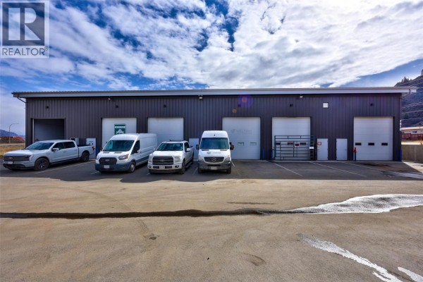 Interior garage bay with equipment, a large vehicle, and an overhead roll-up door. - 7410 Dallas Drive, Kamloops