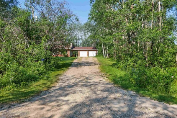 A long gravel driveway winds through trees towards a house with an attached garage visible. - 7415 Twp Road 494 - House B, Rural Brazeau County