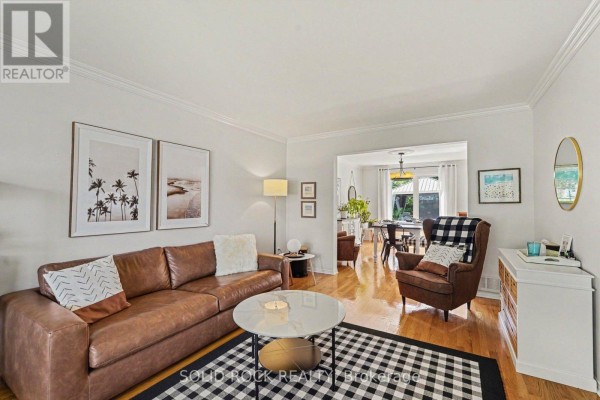 Living room with a brown leather sofa, black and white rug, and view into the dining room and staircase. - 742 Merkley Drive, Ottawa