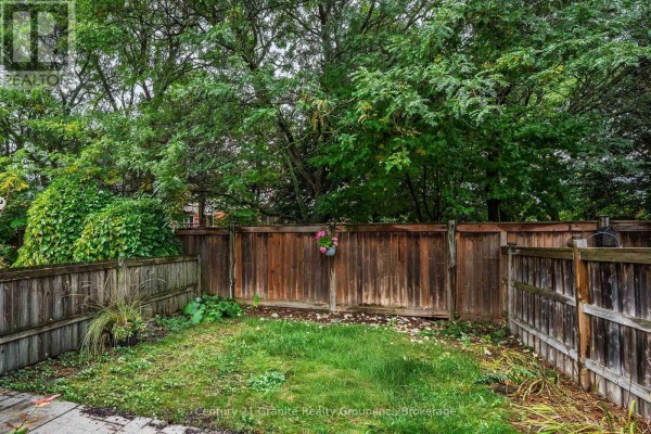 Rear view of a townhouse backyard showing wooden fencing and green trees. - 742 Shanahan Boulevard, Newmarket