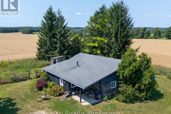 Aerial view of log cabin with grey roof, surrounded by tall evergreen trees and fields. - 742649 Sideroad 4b, Chatsworth