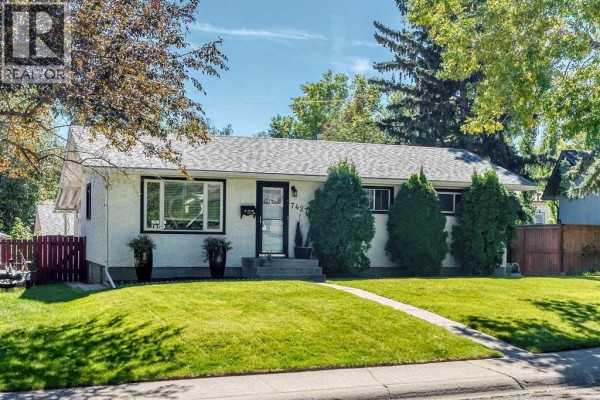 Front view of a modest residential house with white stucco siding and dark trim. - 7427 Fountain Road Se, Calgary