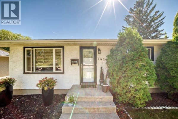 Close-up of the entrance to a house with a white door, large windows, and planters. - 7427 Fountain Road Se, Calgary