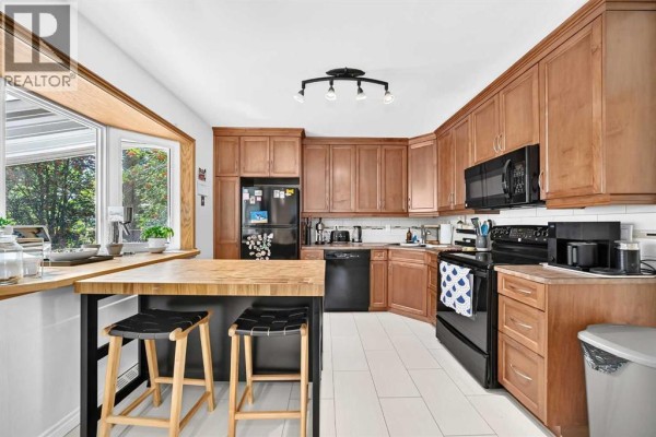 Kitchen with natural wood cabinets, black appliances, white tile floor, and a butcher block island. - 7427 Fountain Road Se, Calgary