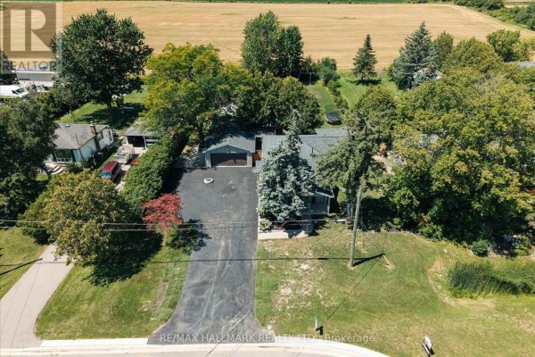 Slightly angled front view of the house and detached garage, with a paved driveway and grass surrounding the property. - 7433 5 Side Road, Halton Hills
