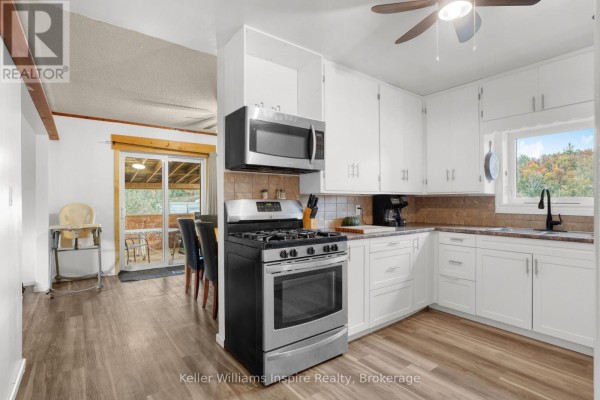 Kitchen with white cabinets, stainless steel gas stove and microwave, granite countertops, and wood-look flooring. - 7437 A Hwy 620, Limerick
