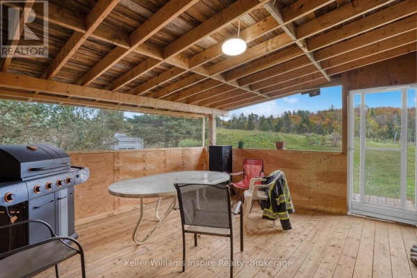 Covered wooden deck with a grill, table, chairs, and views of a rolling green landscape. - 7437 A Hwy 620, Limerick