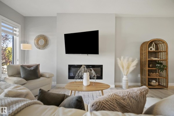 Living room fireplace with a mounted television above and a light-colored sectional couch. - 7437 Creighton Pl Sw, Edmonton
