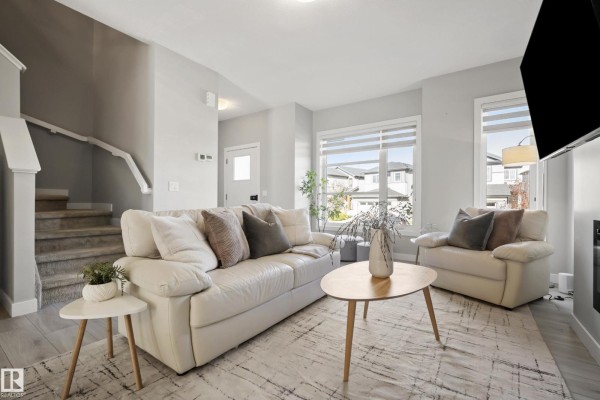 Living room with a white leather couch, armchair, coffee table, fireplace, and light gray walls. - 7437 Creighton Pl Sw, Edmonton